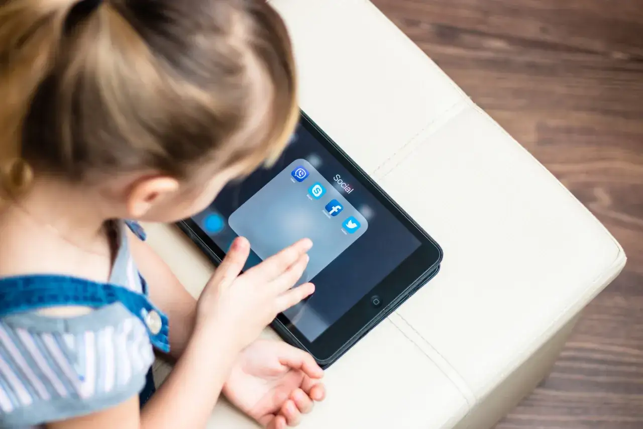 Dziecko dotyka ekranu tabletu z ikonami aplikacji społecznościowych, w tym Facebooka. Ciekawe, od ilu lat jest Facebook?