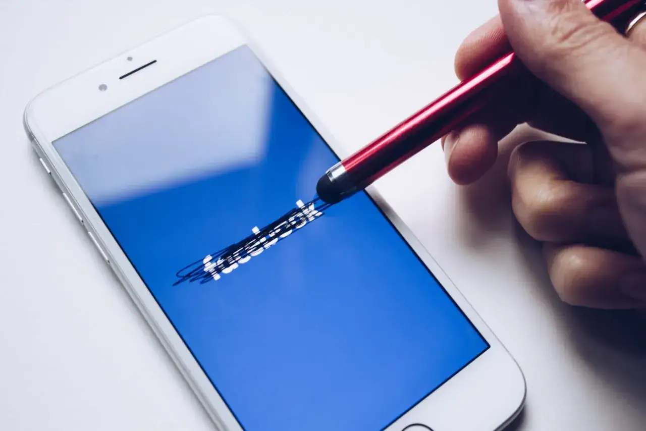 Ręka rysuje czerwonym rysikiem na ekranie telefonu z logo Facebooka. Jak usunąć zdjęcie profilowe na FB?
