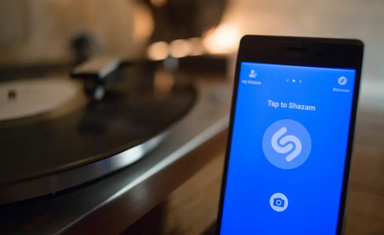 Telefon z aplikacją Shazam gotowy do rozpoznawania muzyki. W tle gramofon.