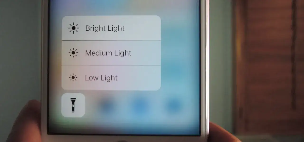 Menu kontrolne iPhone'a z opcjami jasności latarki: Jasne, Średnie, Niskie. Ikona latarki.