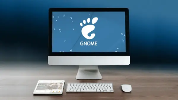 Komputer z logo GNOME, tablet i klawiatura na drewnianym biurku.